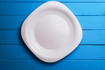 Poster - White plate  on a blue wooden table background.