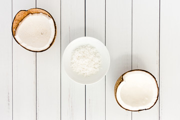 Coconut Halves and Coconut Flakes in a Bowl on White Wood