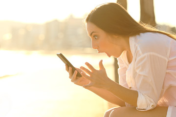 Wall Mural - Amazed girl finding smart phone content on the beach at sunset