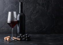 Elegant Glass And Bottle Of Red Wine With Corks And Corkscrew On Black Stone Background. Natural Light