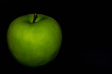 Green ripe apple with water droplets on a dark background, closeup