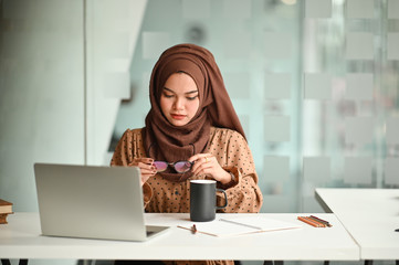 Wall Mural - Islam woman working with laptop and holding a coffee mug and glasses.