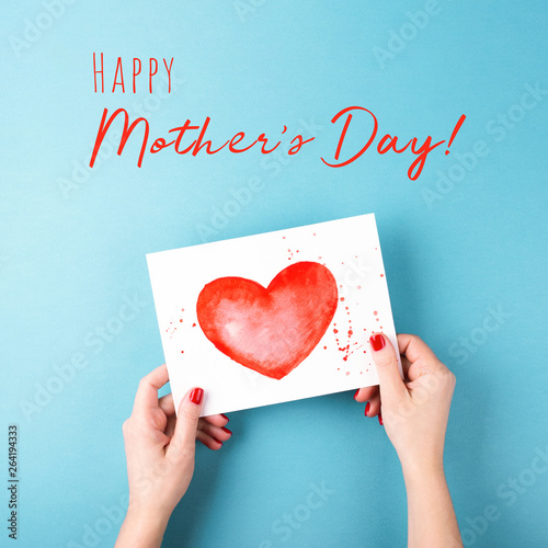 Female's hands holding card with heart on blue background. Happy Mother's Day...