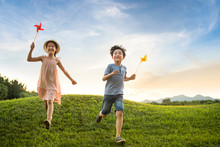 Two Children Playing Paper Windmill On Meadow