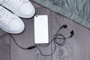 White sneakers with phone, headphones, jacket on grey brown wooden background. Flat lay, copy space.