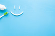 Toothbrush with green bristles, white tube of toothpaste on pastel blue background. Smiley face created from paste. Happy for healthy teeth concept. Empty place for text, quote, sayings or logo. 