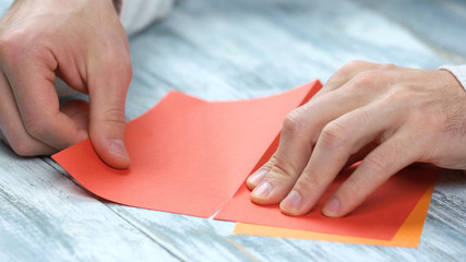 Man creating origami with red paper close up. Male hands dividing paper sheet in half. Paper folding lesson.