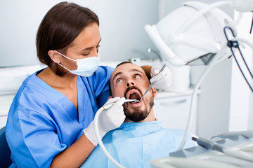 Stomatologist girl in uniform is taking visional inspection of a man