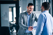 © bnenin - Two smiling businessmen shaking hands while standing in an office.