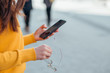 © bnenin - Close-up image of a woman holding eyeglasses and using smart phone in the city street.