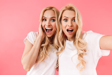 Wall Mural - Surprised happy blonde twins making selfie and looking at camera