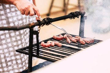 Close up of man hands cooking fresh meat on a old style wood and fire barbecue bbq grill - home celebration for people love to eat and enjoy with friends - restaurant and home cook and food