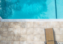 Empty Lounger Chair On A Tile Pool Deck Next To A Clear Blue Swimming Pool With Copy Space