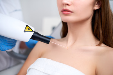 Laser mole removal on a woman's chest in a beauty salon. Hardware cosmetology. Beautician doctor removing birthmark or nevus with laser beam gun in beauty salon. Patient laying on medical chair.