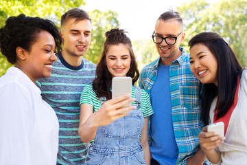 Wall Mural - friendship, technology and international concept - group of friends with smartphone at summer park