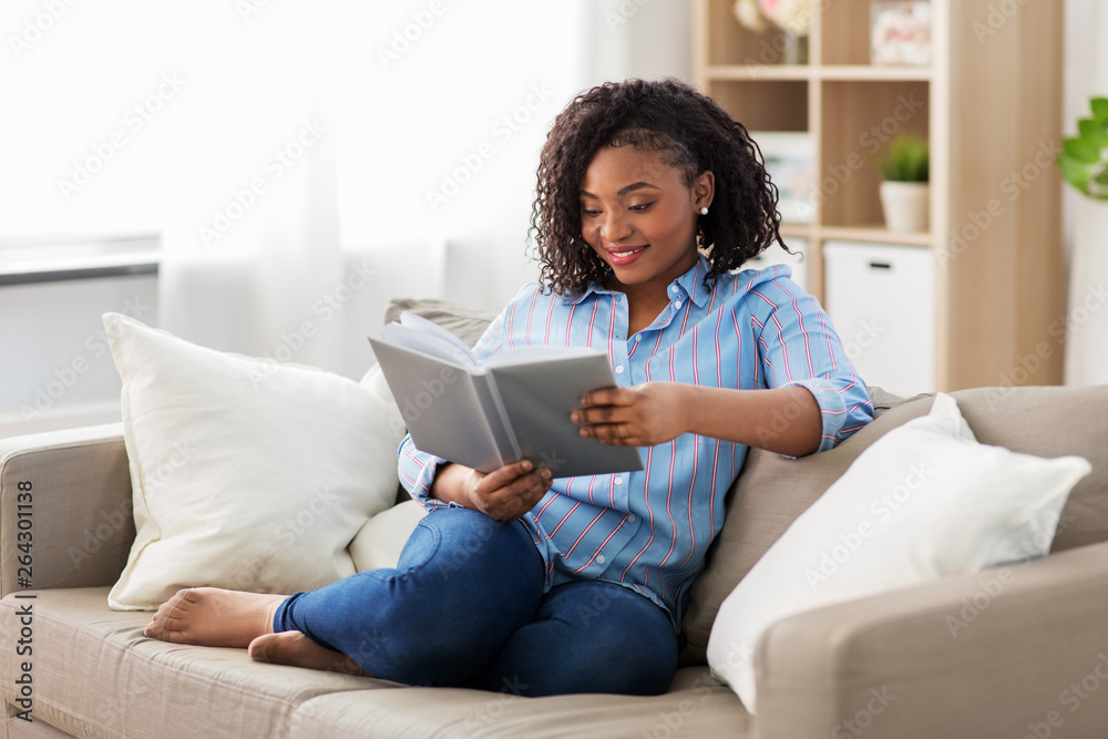 leisure, literature and people concept - smiling african american woman reading book at home - obrazy, fototapety, plakaty 