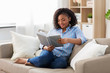 © Syda Productions - leisure, literature and people concept - smiling african american woman reading book at home