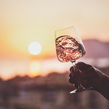 Glass Of Rose Wine In Mans Hand With Sea And Sunset At Background, Close-up, Square Crop. Summer Evening Relaxed Mood Concept
