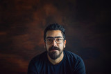 Fototapeta Miasto - Isolated confident  hispanic latin arab indian caucasian middle eastern bearded white man, intellectual nerdy hipster guy, with eyeglasses,in a wooden brown background and plenty of copy-space