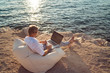 © D'Action Images - Senior man working on his laptop lying on deck chair on the beach during sunset