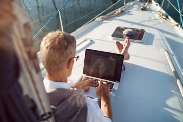 Senior man is working during the vacation on a sailboat