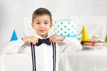 Wall Mural - adorable boy adjusting bow tie and looking at camera during birthday party