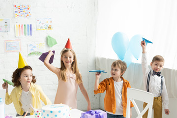 Wall Mural - adorable smiling kids playing with paper planes during birthday party at home