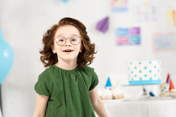 Wall Mural - adorable kid in glasses looking at camera and smiling during birthday celebration at home