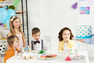 Wall Mural - adorable kids sitting at table and waiting for cake during birthday party