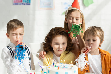 Wall Mural - kids sitting at table with cake and cheering with party horns during birthday celebration