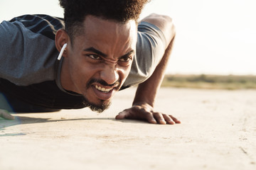 Handsome young african strong sports man listening music with earphones outdoors make exercises.