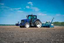 A Large Blue Tractor Prepares The Land For Planting