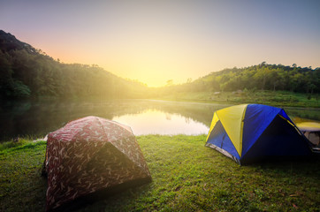 Wall Mural - camping tents in nature background with sunset scenic view at lake and forest pine tree