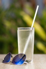 Transparent misted glasses with water and ice against a background of green bushes in different lighting