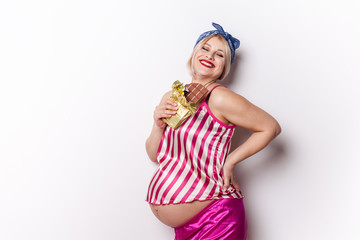 Pregnant adult woman enjoying of eating chocolate bar, copy space. Expectant blonde want some sweetie. Pregnancy whims, unhealthy eating, happiness concept