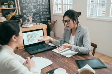 Wall Mural - Business team reviewing document and discussing project. female office workers colleagues arguing at cafe table. angry businesswomen bad teamwork disagree plan chart on laptop computer in coffee shop