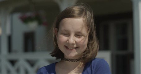 portrait of a child girl looking at the camera and smiling outdoors on sunny day at the house porch 