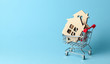 Shopping cart and house on a blue background. Buying and selling real estate. Copy space for text.