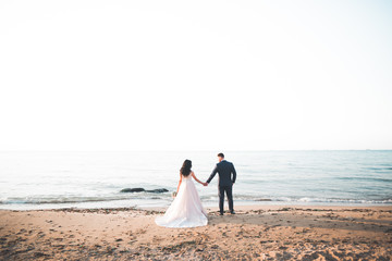 Wedding couple, groom, bride with bouquet posing near sea and blue sky