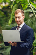 © LIGHTFIELD STUDIOS - smiling businessman in suit and tie using laptop in orangery