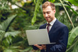 © LIGHTFIELD STUDIOS - smiling businessman in suit and tie using laptop in green orangery