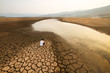 Sad man sit on cracked earth near drying lake in the summer. Climate change and Drought impact concept.