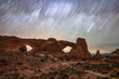 Star trails moving across the night sky over natural sandstone arches. The Windows in Arches National Park. 