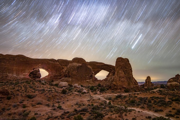 star trails moving across the night sky over natural sandstone arches. the windows in arches nationa