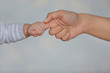 © New Africa - Little baby holding mother's finger on light background, closeup