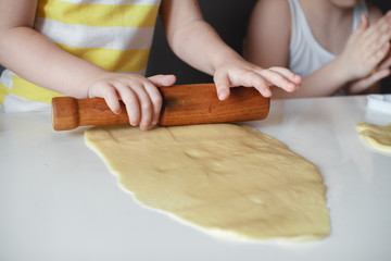 Wall Mural - Little cute girl making shortbread. Rolls out the dough with a rolling pin on a white table. The preparation of the dessert. close-up