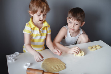 Wall Mural - Two children make cookie mould on a white table. Preparation of homemade dessert