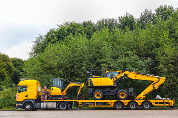 low loader trailer carrying two excavators parking on a public truck parking area of a truck stop.