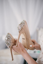 Bride In A White Wedding Dress Holding Wedding Shoes In Her Hands