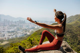 Fototapeta Na drzwi - sexy athletic asian filipino female in workout clothes with her arms raised while sitting on a rock feeling accomplished from hiking lion rock in hong kong on a sunny day